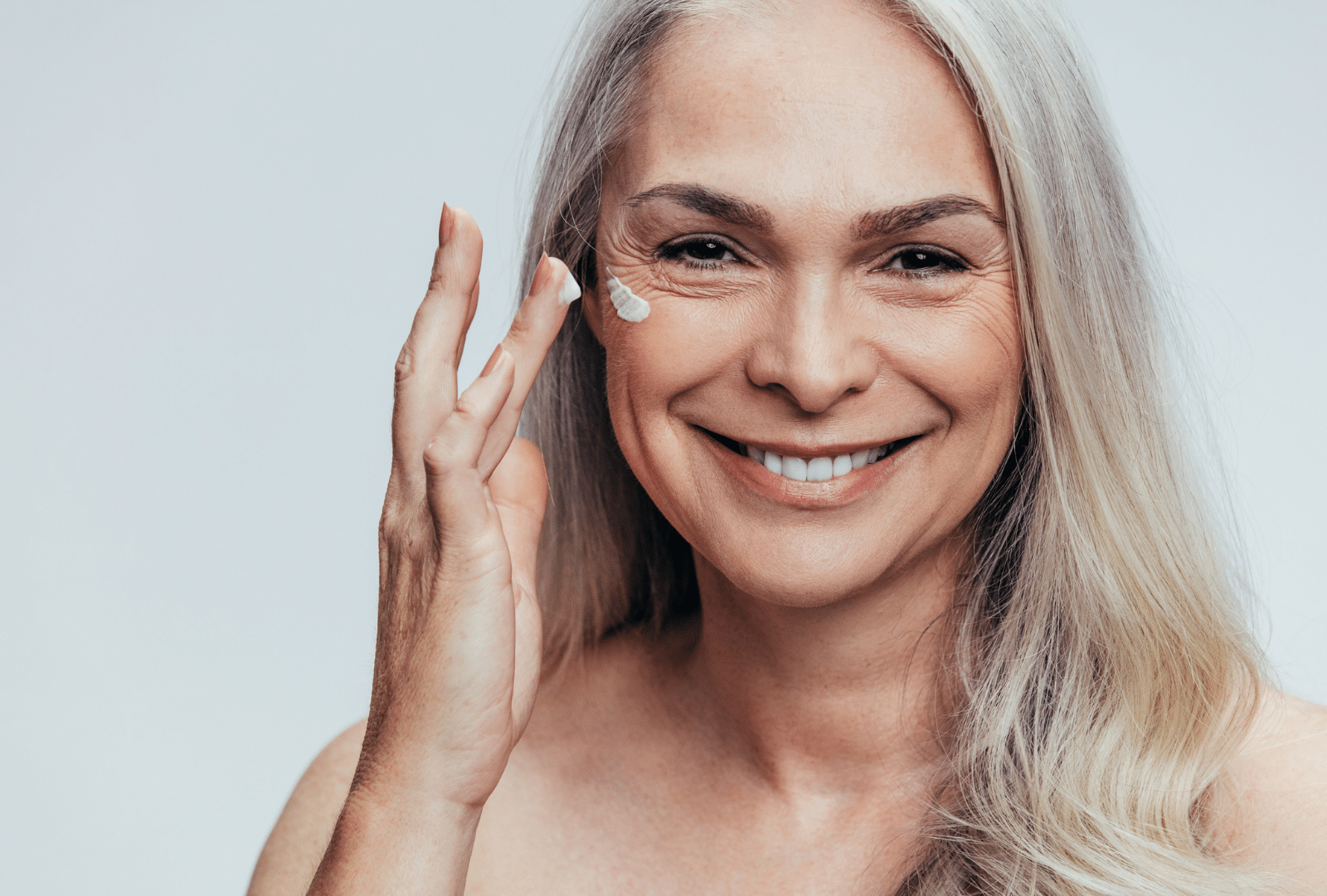 Femme souriante appliquant une crème sur son visage.