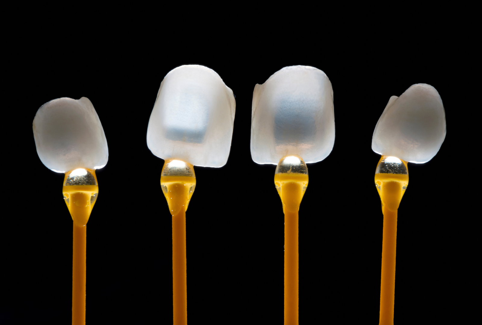 Quatre facettes dentaires illuminés sur fond noir.